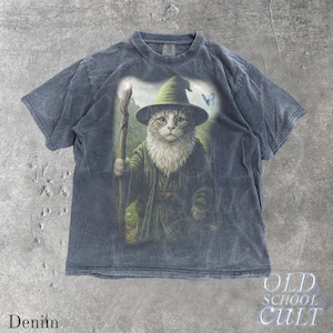 May include: Denim-colored t-shirt featuring a whimsical illustration of a cat dressed as a wizard, complete with a hat, staff, and flowing robes. A blue butterfly is also present in the design. The words "Old School Cult" and "Denim" are printed on the shirt.