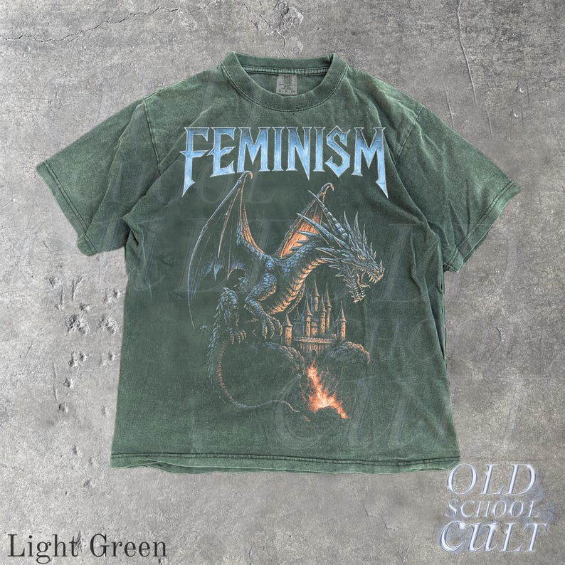 May include: Light green t-shirt with the word "FEMINISM" in a silver, gothic font. A blue dragon graphic is centered below the text, with a castle in the background. The words "OLD SCHOOL CULT" are in the lower right corner.