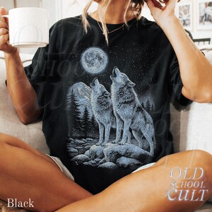 May include: Black t-shirt featuring a graphic of two howling wolves under a full moon and starry night sky. The design includes a forest silhouette and the text "OLD SCHOOL CULT". The shirt is a relaxed fit.