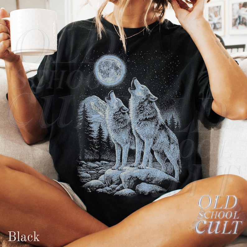 May include: Black t-shirt featuring a graphic of two howling wolves under a full moon and starry night sky. The design includes a forest silhouette and the text "OLD SCHOOL CULT". The shirt is a relaxed fit.