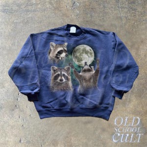 Op de afbeelding: Een marineblauw sweatshirt met een grafische print van drie wasberen die naar een volle maan kijken. De wasberen bevinden zich in een bosrijke omgeving met sterren en wolken op de achtergrond.