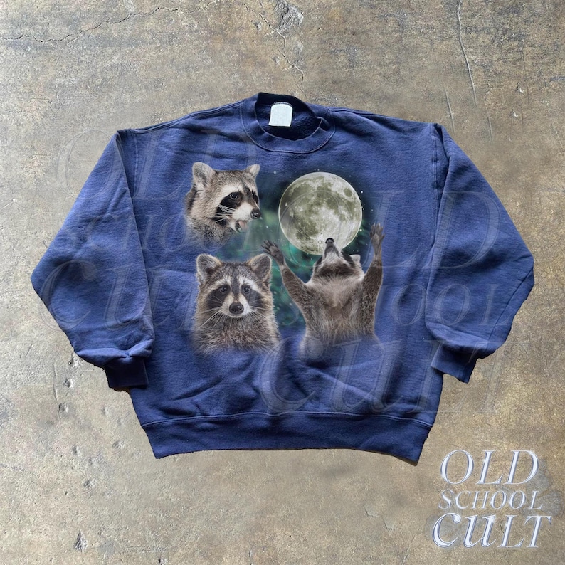 Op de afbeelding: Een marineblauw sweatshirt met een grafische print van drie wasberen die naar een volle maan kijken. De wasberen bevinden zich in een bosrijke omgeving met sterren en wolken op de achtergrond.