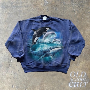 May include: A navy blue sweatshirt with a graphic print of a whale and dolphins jumping out of the water. The graphic is in shades of blue and white.