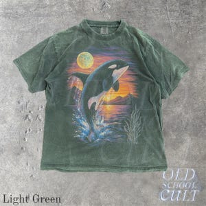Puede incluir: Camiseta verde claro con un gr&aacute;fico de una orca saltando contra un fondo de puesta de sol. El dise&ntilde;o incluye una luna llena, monta&ntilde;as y agua. La camiseta tiene el texto "OLD SCHOOL CULT" y "Light Green".