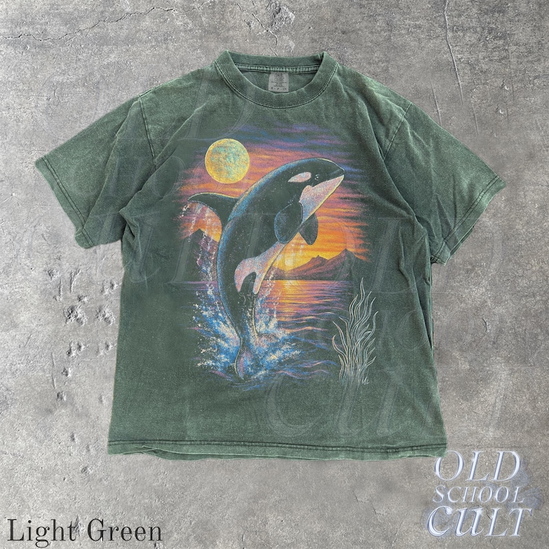 Puede incluir: Camiseta verde claro con un gr&aacute;fico de una orca saltando contra un fondo de puesta de sol. El dise&ntilde;o incluye una luna llena, monta&ntilde;as y agua. La camiseta tiene el texto "OLD SCHOOL CULT" y "Light Green".