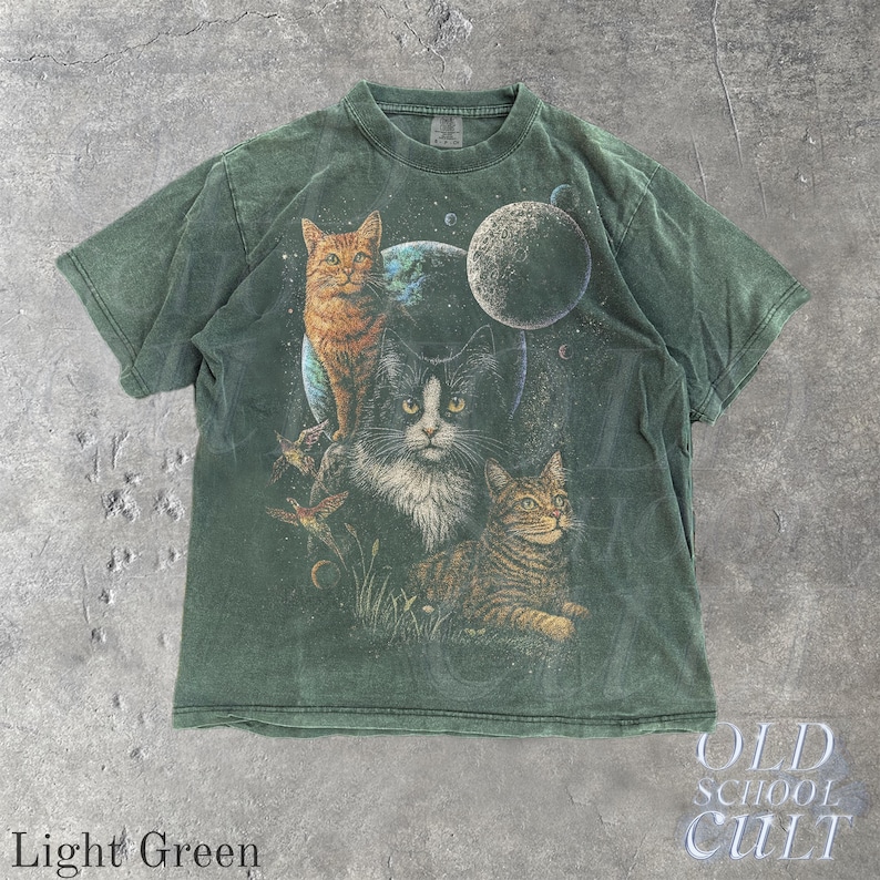 以下が含まれることがあります： 惑星を背景に3匹の猫が描かれた、ライトグリーンのTシャツ。猫はオレンジ、白黒、茶色です。Tシャツには「OLD SCHOOL CULT」と「Light Green」の文字がプリントされています。