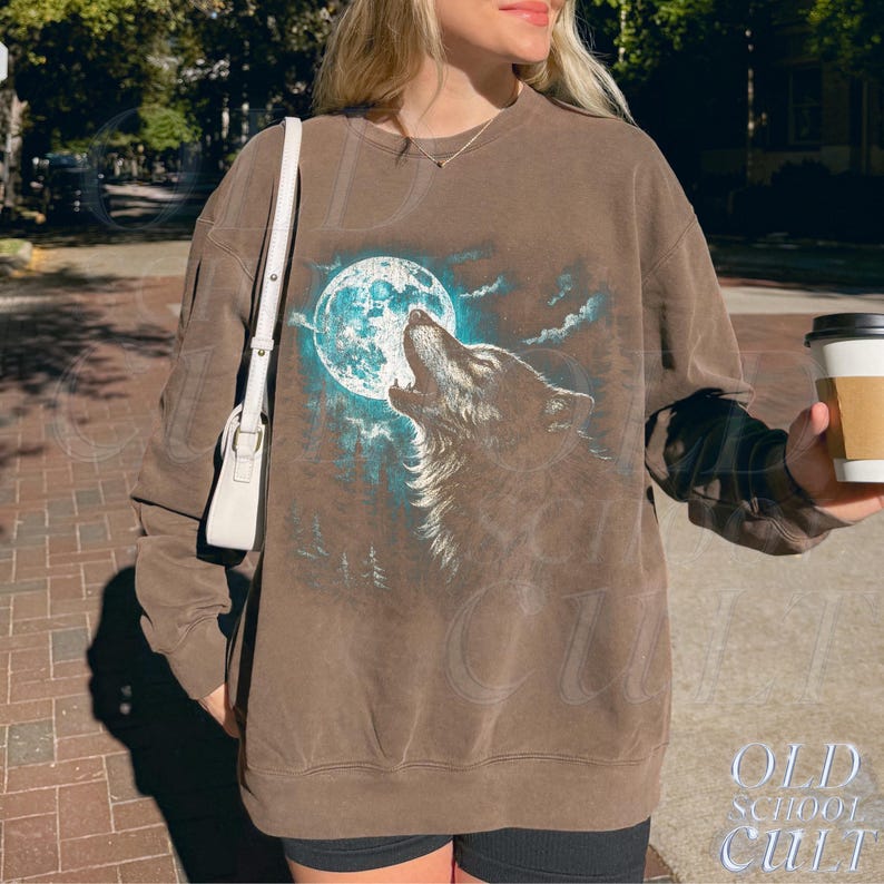 May include: Brown sweatshirt featuring a wolf howling at a turquoise moon. The graphic includes a forest silhouette and clouds. The text "OLD SCHOOL CULT" is printed at the bottom. The sweatshirt is a relaxed fit.