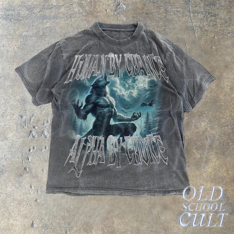 Puede incluir: Camiseta gris oscuro con una ilustraci&oacute;n de hombre lobo y el texto "HUMAN BY CHANCE ALPHA BY CHOICE". El dise&ntilde;o incluye un lobo aullando, un bosque y un cielo tormentoso. La camiseta tiene un aspecto vintage y desgastado.