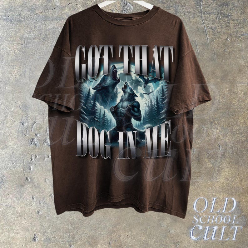May include: Brown t-shirt with a graphic print of two wolves howling at the moon. The text "GOT THAT DOG IN ME" is printed in silver lettering on the front of the shirt.
