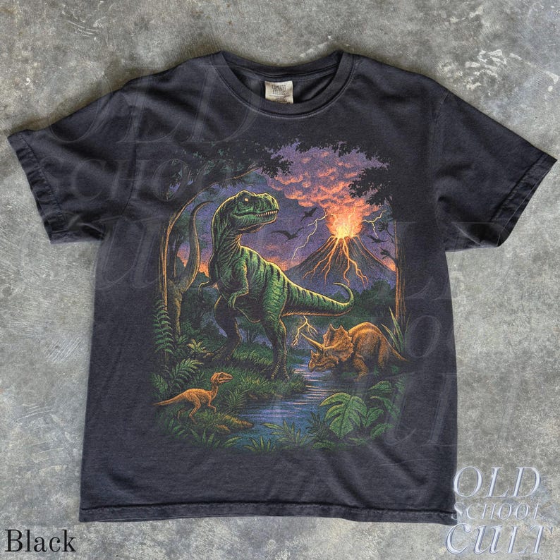 Op de afbeelding: Zwart T-shirt met een dinosaurusontwerp. Het ontwerp toont een groene Tyrannosaurus Rex, een Triceratops en een kleinere dinosaurus in een prehistorisch landschap met een vulkaan. De tekst "OLD SCHOOL CULT" is zichtbaar.