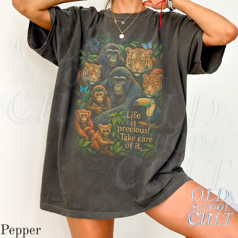May include: Dark grey t-shirt featuring a jungle scene with gorillas, monkeys, tigers, and a toucan. The shirt has the text "Life is precious! Take care of it." printed on the front. The shirt is a relaxed fit.
