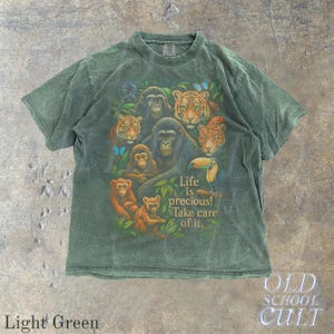 May include: Light green t-shirt featuring a vibrant graphic of various jungle animals, including tigers, gorillas, and monkeys. The text "Life is precious! Take care of it." is also displayed. The shirt is a vintage style.