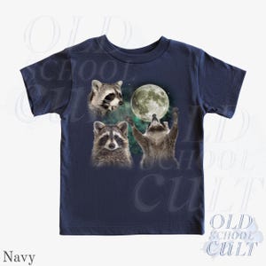 May include: Navy blue t-shirt featuring a graphic of three raccoons with a full moon in the background. One raccoon is looking up at the moon with its arms raised. The text "OLD SCHOOL CULT" is printed on the shirt.