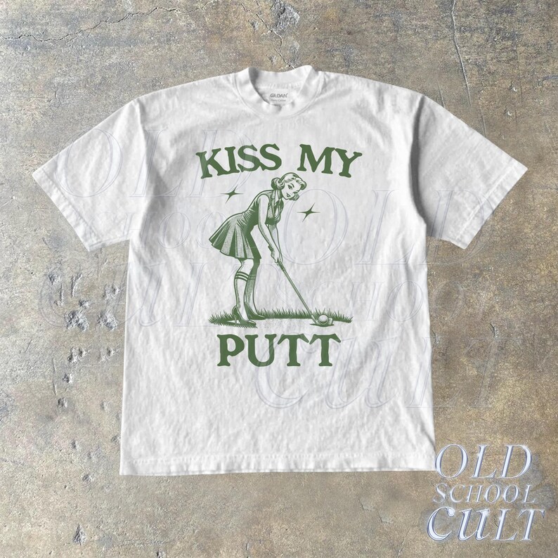 May include: White t-shirt with green text that reads "Kiss My Putt". The graphic features a cartoon woman in a golf outfit putting a golf ball.