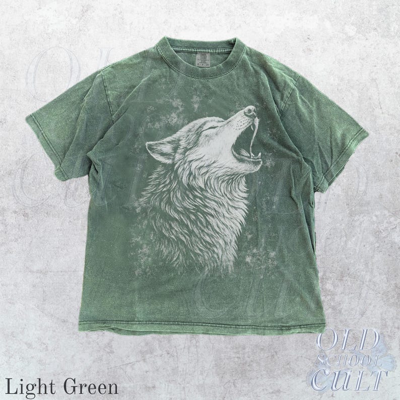 Puede incluir: Camiseta verde claro con una ilustraci&oacute;n blanca de un lobo aullando. La camiseta tiene un aspecto vintage y descolorido. El texto "OLD SCHOOL CULT" est&aacute; en la esquina inferior derecha, y "Light Green" en la inferior izquierda.