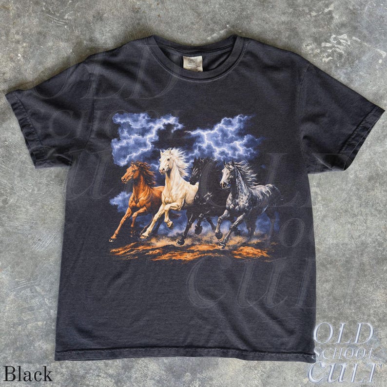 May include: Black t-shirt featuring a graphic of four running horses in shades of brown, white, black, and gray, set against a backdrop of a stormy sky with lightning. The shirt has a crew neck and short sleeves.