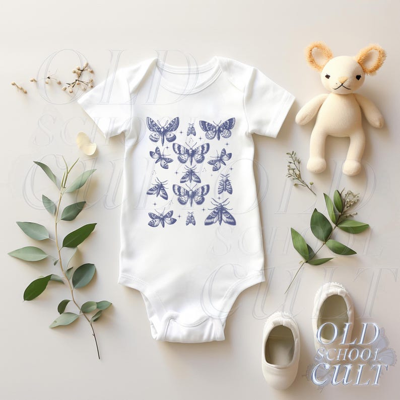 May include: White baby onesie with a blue butterfly pattern. The short-sleeved bodysuit features a collection of stylized butterflies in various sizes and designs. The image is styled with a plush toy, baby shoes, and greenery.