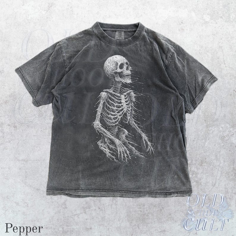 May include: Pepper-colored t-shirt featuring a detailed white skeleton graphic. The design is centered on the front of the shirt, with the skeleton's rib cage and limbs visible. The shirt has a vintage, worn look.