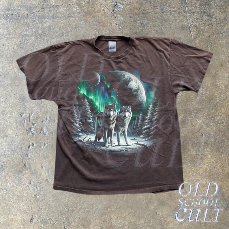 May include: A brown t-shirt with a graphic print of two wolves howling at the moon. The wolves are surrounded by a green and blue aurora borealis. The shirt has a faded look and is made of a soft, comfortable material.