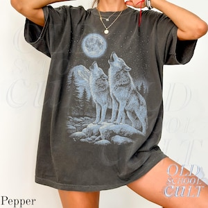 May include: Dark gray t-shirt featuring a graphic of two wolves howling at a full moon in a starry night sky. The design includes a mountain range and forest. The shirt has a vintage, worn look and the text "OLD SCHOOL CULT" is visible.
