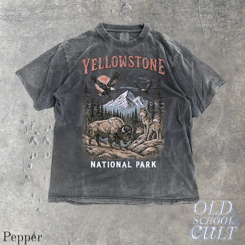 May include: A charcoal gray t-shirt featuring a Yellowstone National Park design. The graphic includes a bison, wolves, eagles, mountains, and the text "YELLOWSTONE NATIONAL PARK". The shirt has a vintage, worn look.