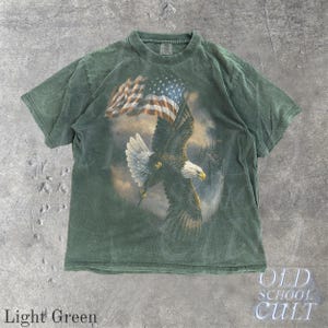 May include: Light green t-shirt with a graphic of an eagle and the American flag. The eagle is in flight. The shirt has a faded appearance. The text "OLD SCHOOL CULT" is printed on the bottom right. The words "Light Green" are printed on the bottom left.