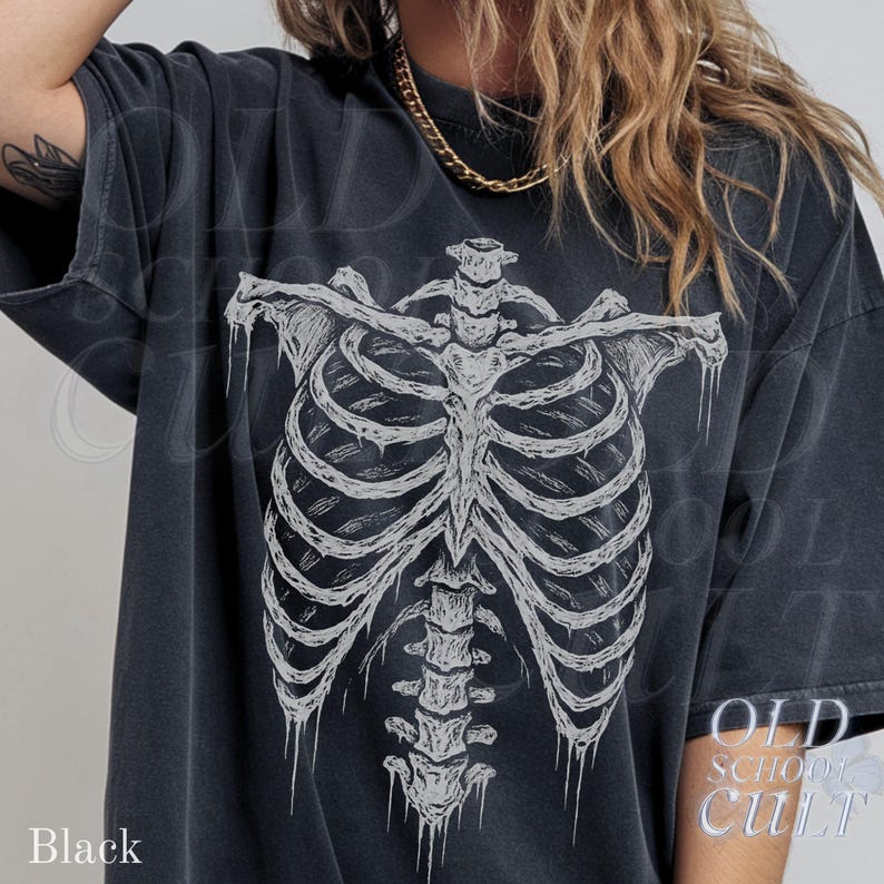 May include: Black oversized t-shirt featuring a detailed white skeletal rib cage graphic. The shirt has a vintage, worn look. The text "OLD SCHOOL CULT" is printed on the lower right side of the shirt. The word "Black" is printed on the lower left side.