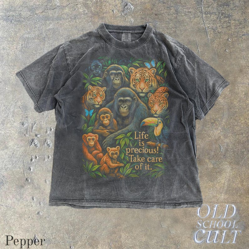 May include: Dark gray t-shirt featuring a colorful jungle scene with gorillas, tigers, monkeys, and a toucan. The shirt has the text "Life is precious! Take care of it." The shirt is from the Old School Cult brand.