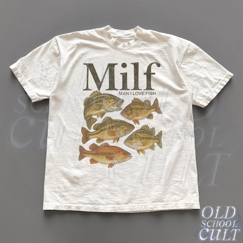 May include: White t-shirt with a graphic of six fish in shades of brown and orange. The word "Milf" is printed above the fish, with "Man I Love Fish" below. The shirt has a crew neck and short sleeves.