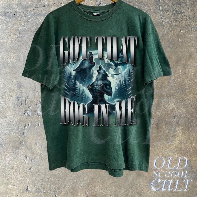 May include: Green t-shirt with a graphic print of two wolves howling at the moon. The text "GOT THAT DOG IN ME" is printed on the shirt.