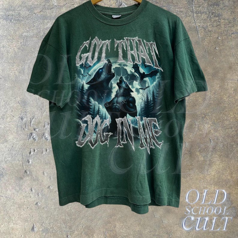 K&ouml;nnte beinhalten: Gr&uuml;nes T-Shirt mit einem Grafikdruck von zwei W&ouml;lfen, die zum Mond heulen. Der Text "GOT THAT DOG IN ME" ist in silbernem Glitzer auf der Vorderseite des Shirts gedruckt.