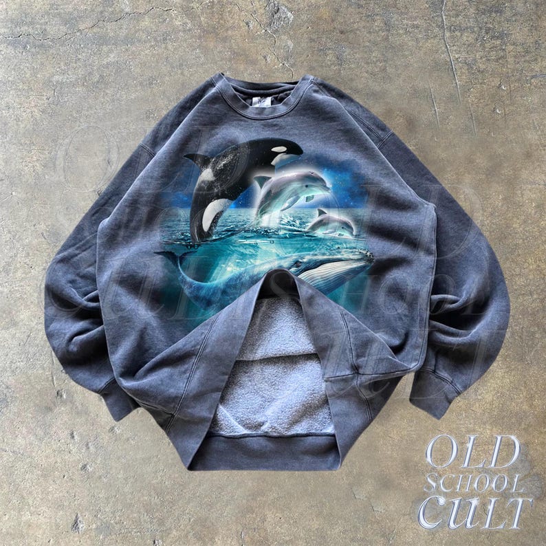 May include: A dark gray sweatshirt with a graphic print of a pod of dolphins and whales jumping out of the water. The sweatshirt has a crew neck and long sleeves.