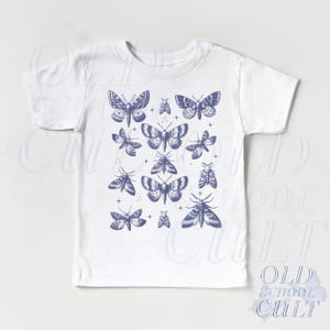 May include: White t-shirt featuring a collection of blue moth illustrations. The moths are in various sizes and poses, creating a detailed and artistic design. The shirt is a classic crew neck style.