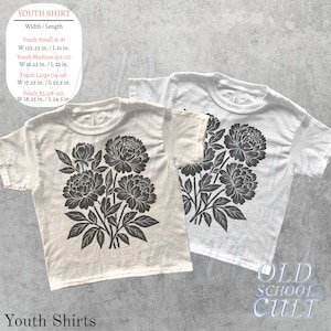 May include: Two youth shirts, one cream and one white, each with a black floral design. The cream shirt is on the left, and the white shirt is on the right. The shirts have a crew neck and short sleeves. The text "Youth Shirts" is at the bottom.