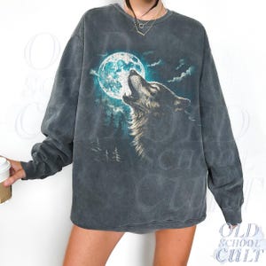 May include: Dark gray sweatshirt featuring a wolf howling at a full moon. The graphic is in shades of blue, white, and gray. The sweatshirt has a vintage, washed look. The text "OLD SCHOOL CULT" is printed on the bottom right.