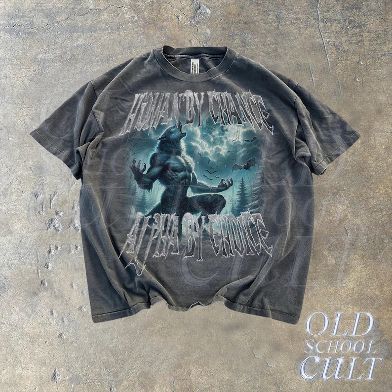 Puede incluir: Camiseta gris oscuro con un dise&ntilde;o de hombre lobo y el texto "HUMAN BY CHANCE ALPHA BY CHOICE". El dise&ntilde;o incluye un lobo aullando bajo un cielo tormentoso y un bosque. La camiseta tiene un aspecto vintage.