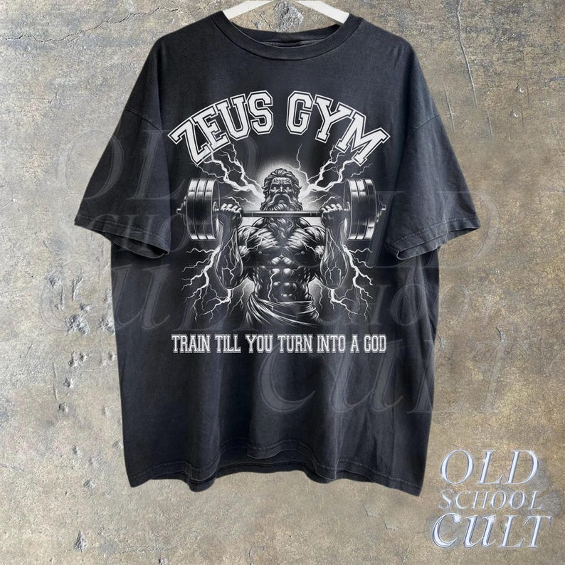May include: Black t-shirt with a white graphic of a muscular figure lifting a barbell. The graphic includes the text "Zeus Gym" and "Train till you turn into a god."