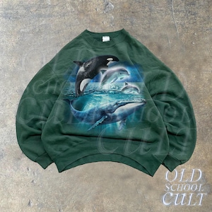 May include: A dark green sweatshirt with a graphic print of dolphins and a whale swimming in the ocean. The graphic is in shades of blue and white.