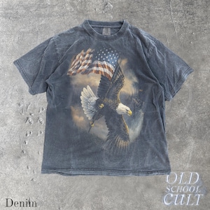 May include: A denim-blue t-shirt with a print of a bald eagle and an American flag. The eagle is in flight, with a misty landscape in the background. The shirt has a faded look. The words "OLD SCHOOL CULT" are printed on the bottom right.