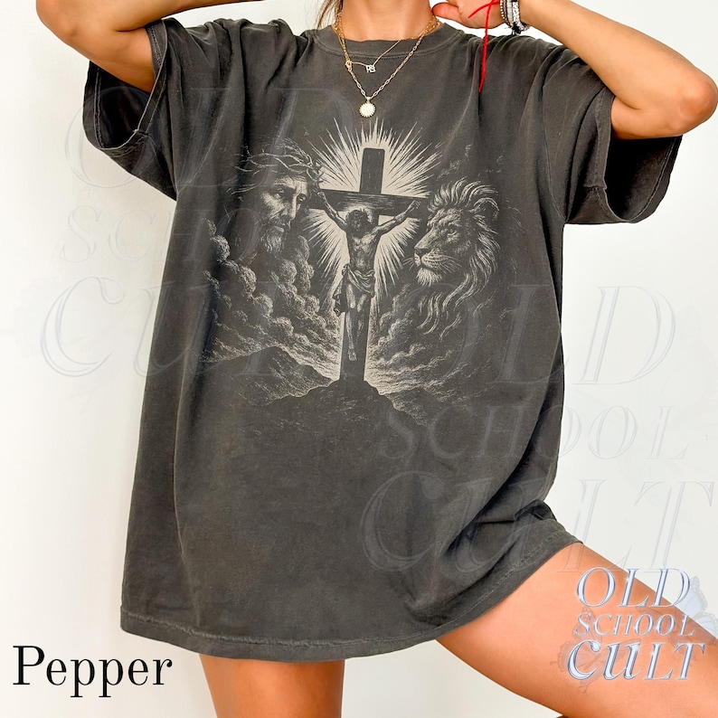 May include: Dark gray t-shirt featuring a religious graphic. The design includes a depiction of Jesus on the cross, a lion, and a man with a crown of thorns. The word "Pepper" is printed at the bottom left.