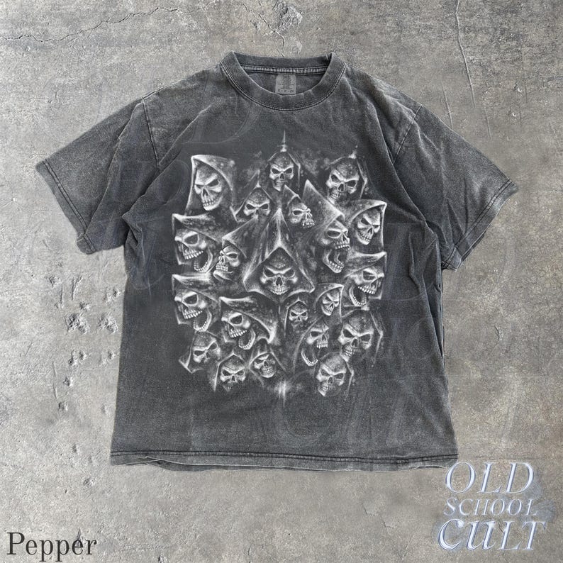 以下が含まれることがあります： 複数のフード付きの頭蓋骨が描かれた、濃いグレーのTシャツ。デザインはグレーと白の濃淡で、印象的なコントラストを生み出しています。「OLD SCHOOL CULT」の文字が右下に表示されています。