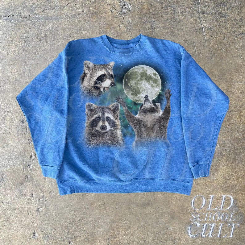Op de afbeelding: Een blauw sweatshirt met een grafische print van drie wasberen die naar een volle maan kijken. De wasberen zijn in een realistische stijl en de maan is wit met een lichtblauwe gloed.