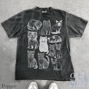 May include: Dark gray t-shirt featuring a collection of illustrated cats in various poses. The shirt has a crew neck and short sleeves. The text "OLD SCHOOL CULT" is printed on the lower right side of the shirt.