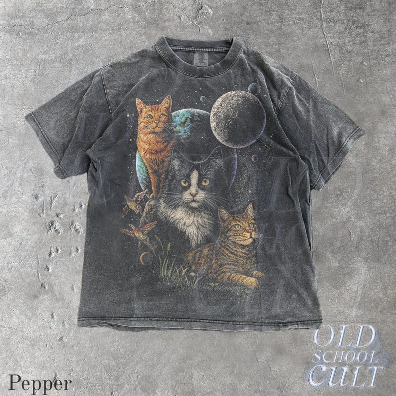 以下が含まれることがあります： 宇宙にいる3匹の猫のグラフィックが特徴の濃い灰色のTシャツ。猫はオレンジ色、白と黒、茶色のトラ柄です。シャツには「Pepper」と「OLD SCHOOL CULT」の文字が入っています。