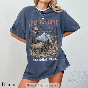 May include: Denim blue t-shirt with a graphic of Yellowstone National Park. The design features a bison, wolves, mountains, and eagles. The text "Yellowstone National Park" is displayed in a vintage style.