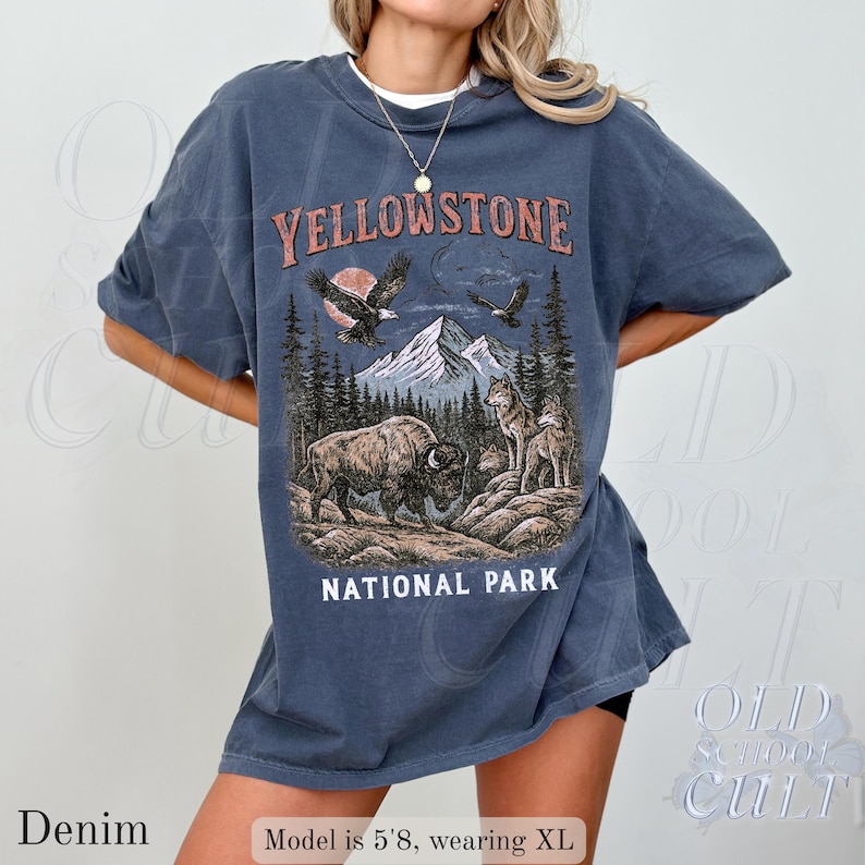 May include: Denim blue t-shirt with a graphic of Yellowstone National Park. The design features a bison, wolves, mountains, and eagles. The text "Yellowstone National Park" is displayed in a vintage style.
