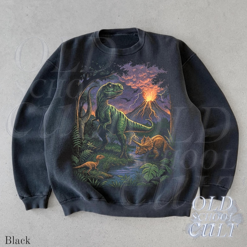 Op de afbeelding: Zwarte crewneck sweatshirt met een gedetailleerde dinosaurus illustratie. Het ontwerp toont een groene T-Rex, een Triceratops en een vulkaan onder een stormachtige hemel. De tekst "OLD SCHOOL CULT" staat rechtsonder.
