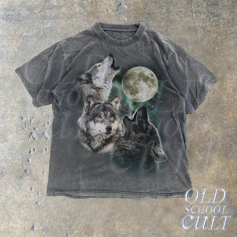 Könnte beinhalten: Ein graues T-Shirt mit einem grafischen Aufdruck von drei Wölfen, die zum Mond heulen. Die Wölfe befinden sich in einer dunklen Waldkulisse mit einem sternenklaren Himmel.