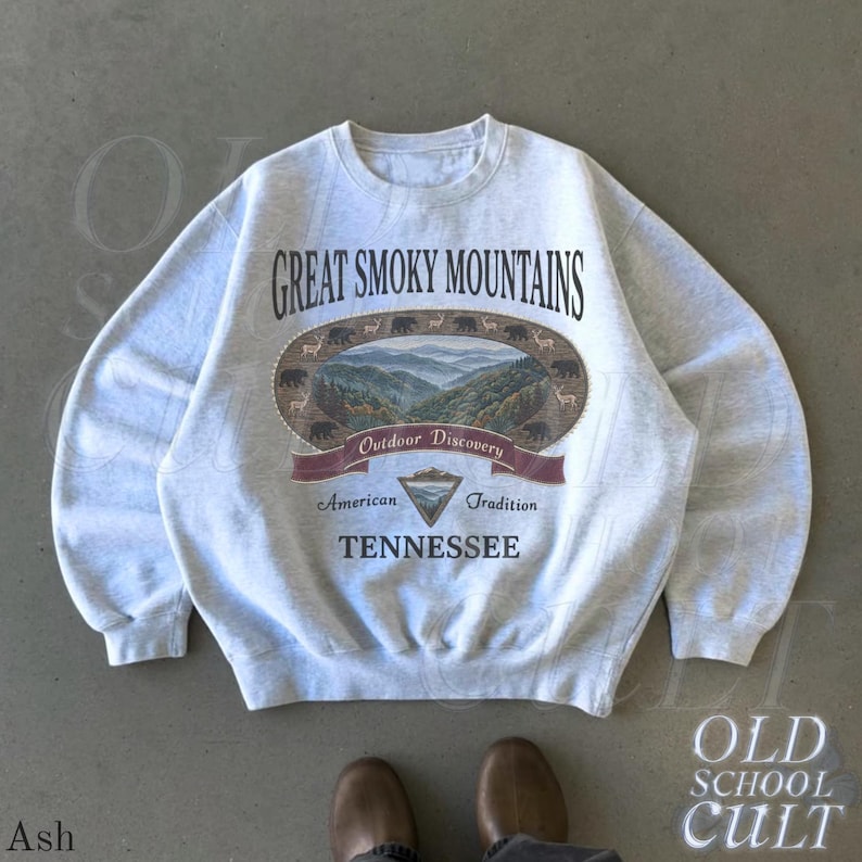 K&ouml;nnte beinhalten: Hellgraues Sweatshirt mit dem Schriftzug "Great Smoky Mountains" und einer Grafik einer Berglandschaft. Das Sweatshirt tr&auml;gt auch die Worte "Outdoor Discovery", "American Tradition" und "Tennessee".