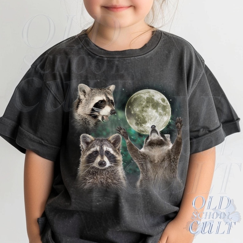 May include: Dark gray t-shirt featuring a whimsical design of three raccoons and a full moon. One raccoon is howling, another is looking up, and the third is looking forward. The text "OLD SCHOOL CULT" is printed on the bottom right.